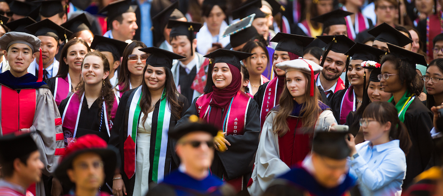 Image of graduates smiling in the audience in their full regalia