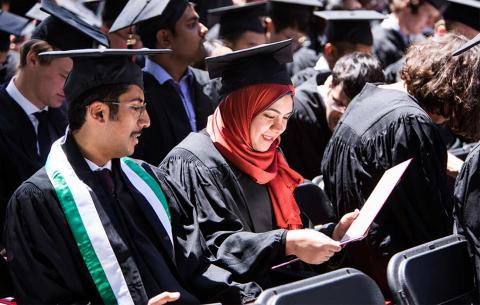 Graduates look at their diplomas while seated in the audience