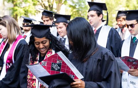 Image of two female graduates holding and smiling at the 2023 OneMIT Commencement Ceremony trifold program