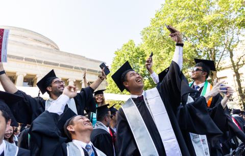 Image of 2023 graduates smiling and taking a group selfie in front of the Killian Court stage